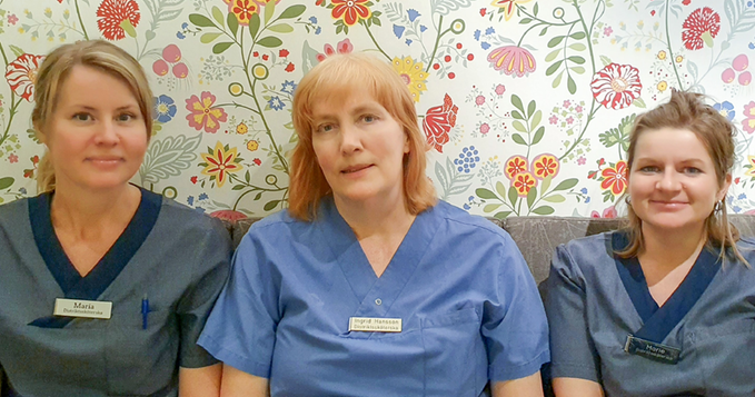 Tre personer som sitter ner bredvid varandra mot en vägg med en blommig tapet.