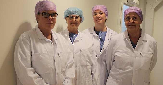Fyra personer klädda i operationskläder står tillsammans och tittar in i kameran