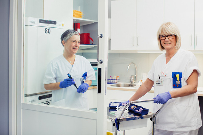 Två personer arbetar i vita vårdkläder och blå plasthandskar i ett labb.