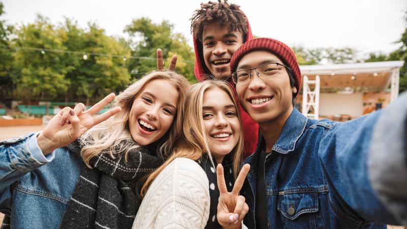 Fyra leende ungdomar som tar en selfie i utomhusmiljö.
