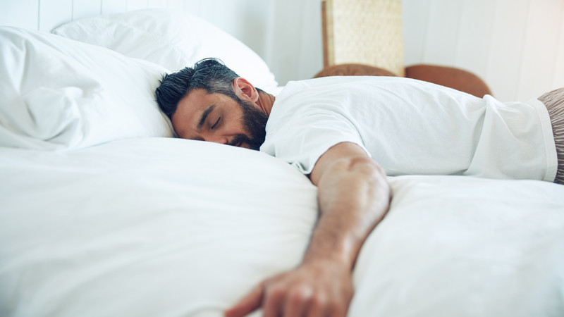Vuxen person sover på mage i en säng.