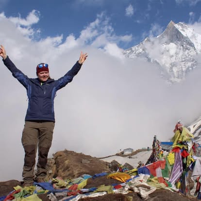 En person står uppe på ett berg, i bakgrunden syns en snöig bergstopp, på marken ligger tibetanska böneflaggor i olika färger.
