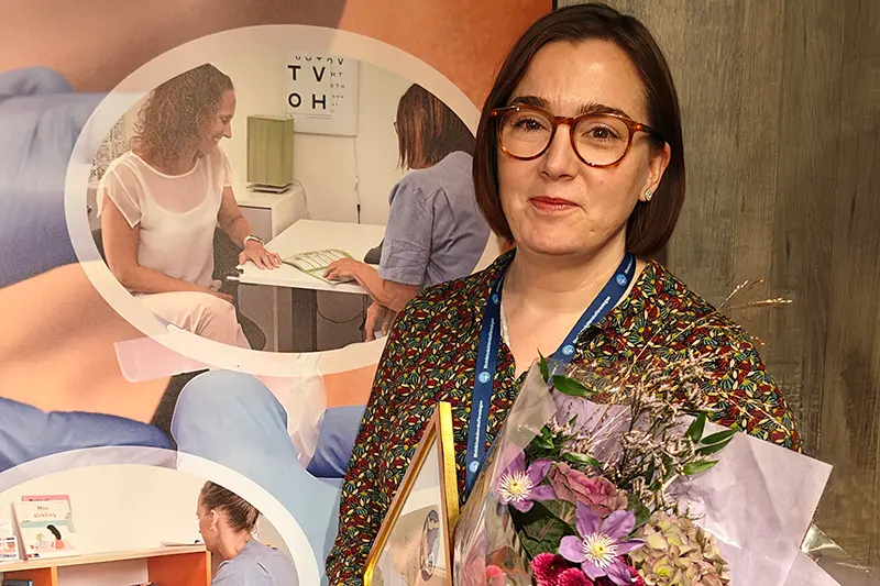 Person i glasögon och med mörkt hår i pagefrisyr. I famnen har personen en blombukett och ett diplom.