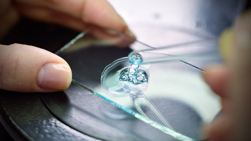Ett par händer pressar ut en vätska ur en pipett på en glasskiva.