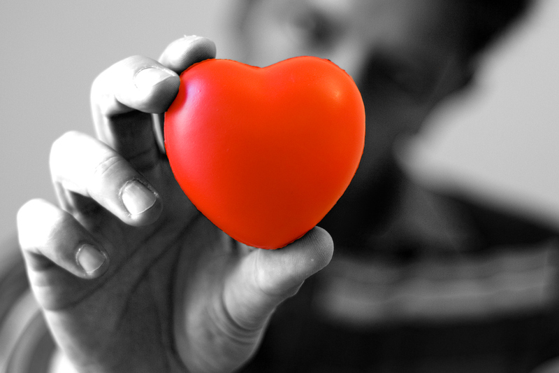 Svartvit bild på en hand som håller ett rött hjärta