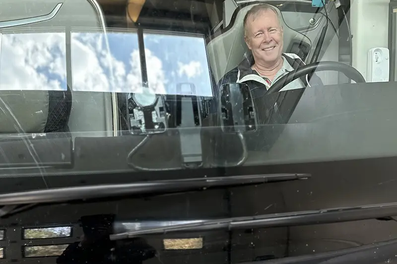 En leende person sitter bakom ratten i en ambuss