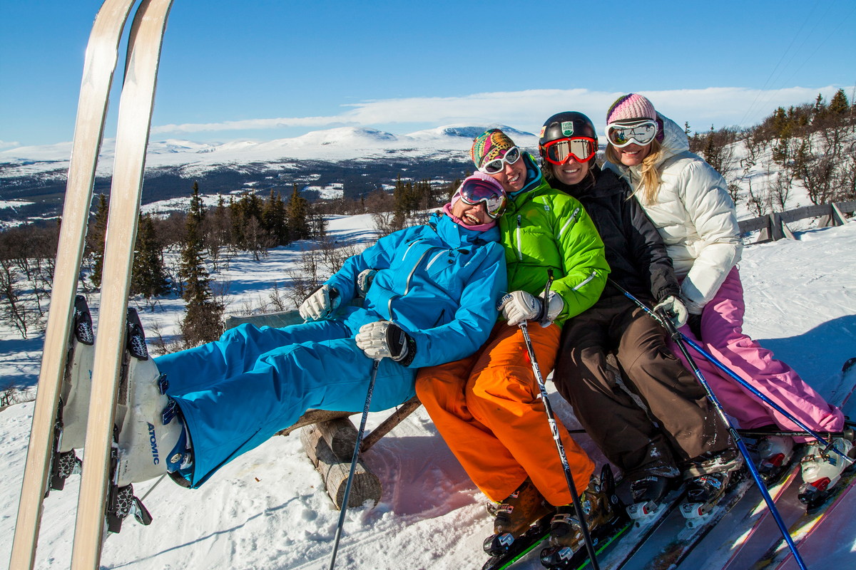 Fyra stycken unga vuxna i slalombacken, poserande framför kameran halvsittande i varandras knän. 
