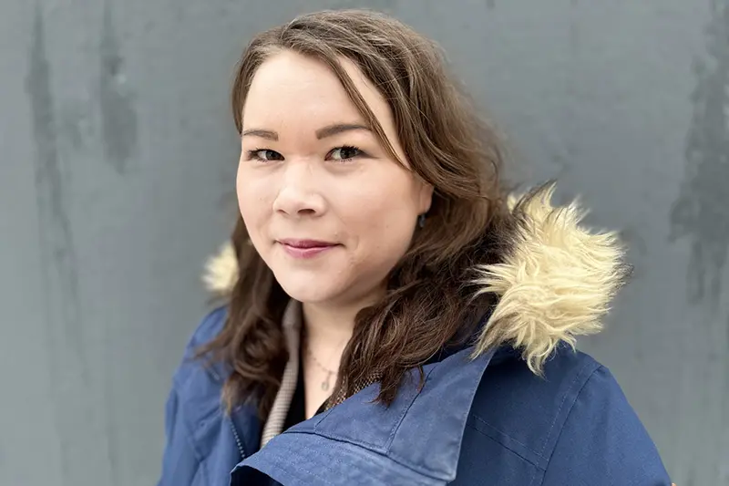 Närbild på person med axellångt mörkt hår och vinterjacka med huva