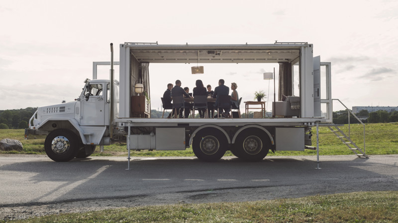 Människor har konferens runt ett bord i en lastbil utomhus, med öppna väggar. Symboliserar att jobba mobilt, på distans.