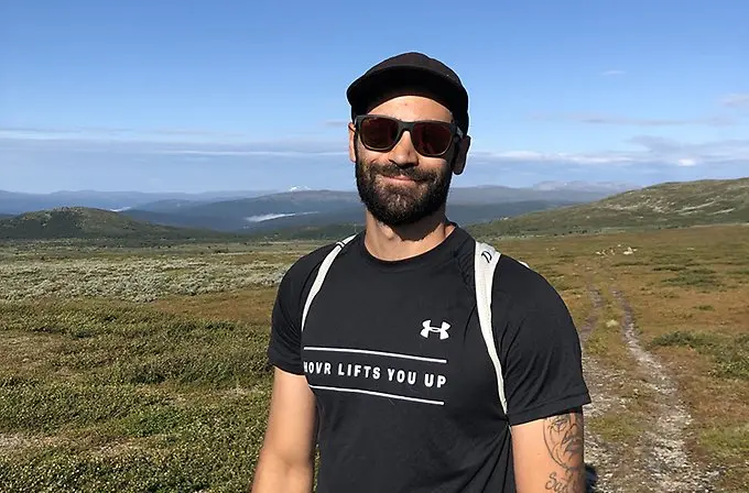 En leende person med solglasögon i somrig fjällmiljö