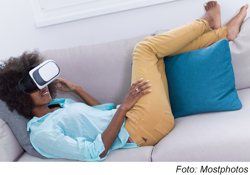 Kvinna som ligger i soffan med VR-glasögon på Foto Mostphotos
