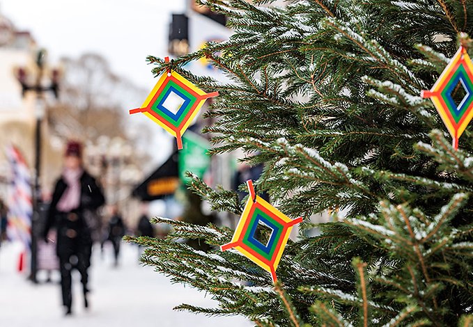Närbild på en julgran utsmyckad med fyrkantiga symboler i de samiska färgerna. Gult, rött, grönt och blått. I den suddiga bakgrunden anas människor som går längs en gata i stadsmiljö.