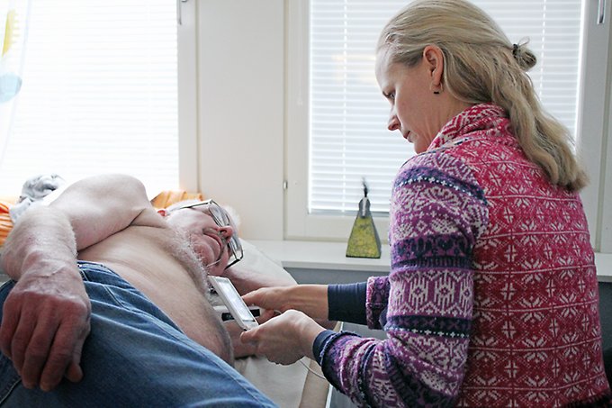 en man ligger på sidan på en brits med bar överkropp och får hjärtat undersökt med ultraljud av en kvinnlig läkare som sitter på en pall bredvid britsen.