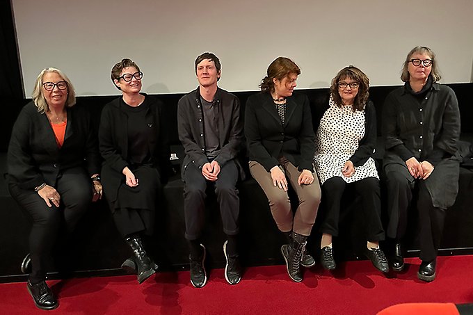Sex personer sitter i rad på en scen