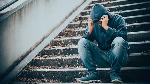 En person sitter i en trappa och tittar ledset ner i knäna.
