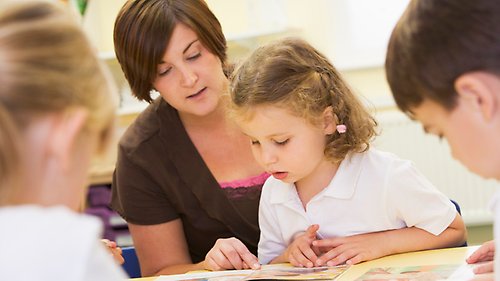 Tre barn som läser tillsammans med en vuxen.