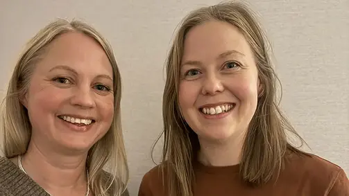 Två personer står bredvid varandra framför en vit vägg.