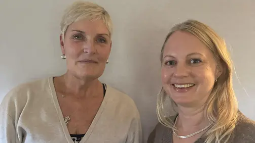 Två personer står bredvid varandra framför en vit vägg.