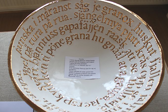 En stor keramikskål i vitt och guld med text på jamska inuti