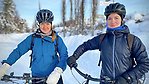 Två personer står och håller i varsin cykel i ett vinterlandskap och tittar mot fotografen