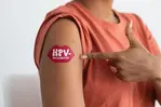Person i halvbild pekar på sin högra överarm där det sitter ett plåster som är format som en röd mun vari det står HPV-vaccinerad.